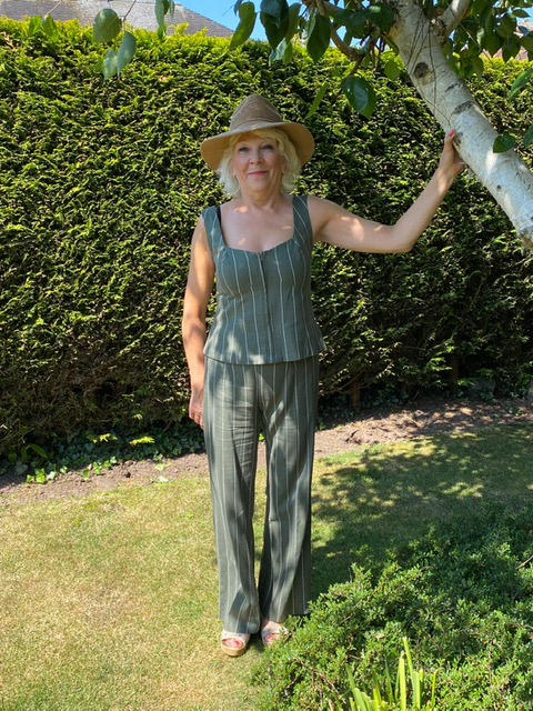 Paula stood under tree in garden wearing olive stripe linen matching trousers and top