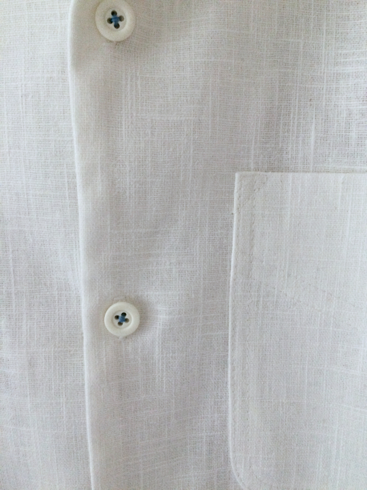 contrast pale blue thread used to sew on the buttons of a simple man's white ramie fibre shirt